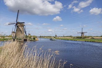 Windmills and a boat on a river under a blue sky with white clouds, many historic windmills on a