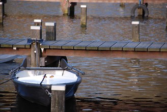 A single boat is moored to a small jetty on the calm waters of a spring lake, rowing boats and