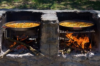Close-up of two paella pans cooking a typical paella from valencia, spain on a barbecue in the