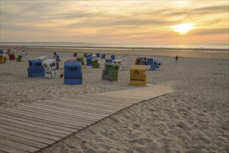 A quiet beach with colourful beach chairs and a wooden jetty at sunset, Sunset on a beach with