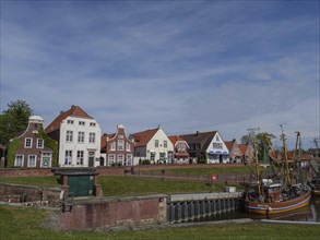 Houses in different colours and styles stand along a canal under a blue sky. A traditional boat in