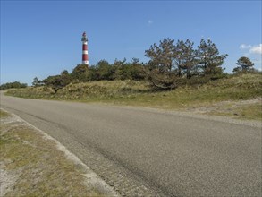 Country road leads to a red and white lighthouse next to trees under a clear sky, red and white