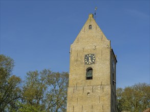 Brick church tower with clock face and surrounding trees under a clear blue sky, church tower on