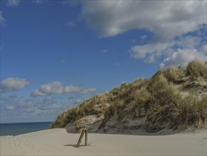 High sand dunes with grass, behind them the sea and a partly cloudy sky, dunes on an island with a