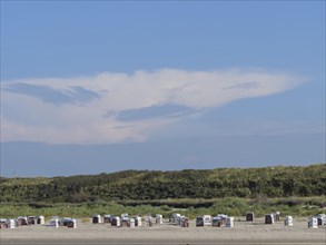 Beach with many beach chairs in front of large dunes, impressive cloud formation in the sky, dunes