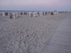 Wooden path along the beach with many empty beach chairs at dusk and clouds, setting sun on a beach
