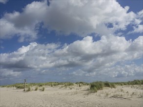 Wide sand dune landscape under a partly cloudy sky, quiet atmosphere, lonely beach with dune grass