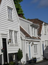 Narrow alley with white wooden houses with red tiled roofs and flowering plants, white wooden
