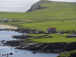 A peaceful coastal landscape with green hills, a house and sea view, green meadows on a deep blue