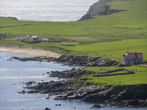 Sea view with green hills, cliffs and a lonely house, green meadows on a deep blue sea and a rocky