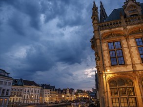 Illuminated gothic buildings and a canal at night under a dramatic sky, historic buildings with