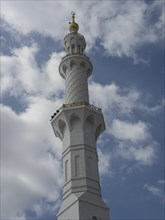 Close-up of an ornate mosque minaret against a cloudy sky, large mosque with white domes and large