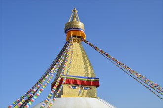 Top part of Boudhanath Stupa or Chaitya adorned with colorful prayer flags under a clear blue sky