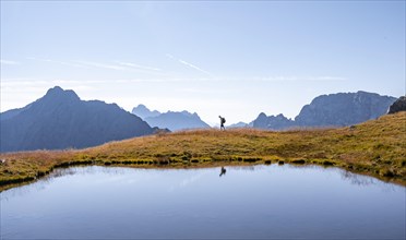 Mountaineer reflected in lake in front of mountain landscape, mountain lake and silhouettes of
