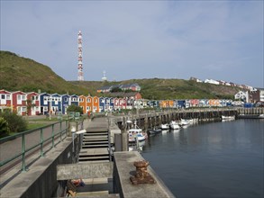 Colourful houses at the harbour, boats in the calm water, green hills in the background under a
