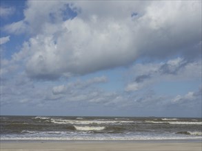 View of the wavy sea and the cloudy sky over the sandy beach, waves on a beach, sunny day with