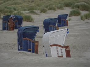 Several blue and white beach chairs on the quiet beach in front of the dunes, colourful beach