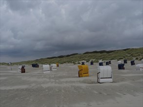 Several beach chairs on the sandy beach in front of the dunes under a grey sky, colourful beach