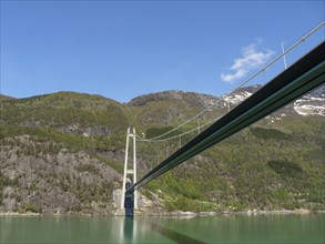 Floating bridge over wooded slopes, under a clear blue sky, bridge in a fjord with snow-capped