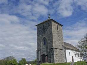 Historic stone church tower surrounded by blooming nature and a clear blue sky, old stone church