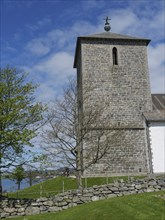 Stone church tower in a natural environment with trees and blue sky, old stone church and many