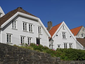 White painted houses with red tiled roofs and flower beds in the front garden, blue sky, stone wall