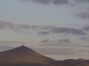 Mountain with antennas on the summit, surrounded by clouds in the soft light of dusk, barren