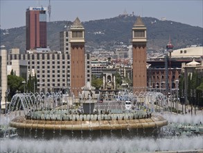 City view with central fountain and historical towers and modern buildings surrounded by mountains,