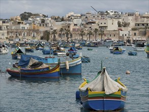 View of a multitude of fishing boats in a busy harbour off the coast of a town, many colourful