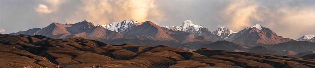 Snow-covered and glaciated mountain peaks at sunset, autumnal hills with brown grass, Issyk Kul,
