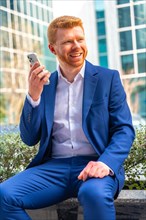 Vertical portrait of a happy businessman talking to the mobile sitting outdoors