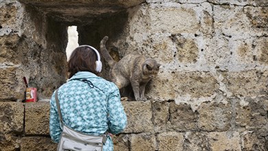 Woman feeding a cat on an old stone wall, near Grand Master's Palace, Knights' Town, Rhodes Town,
