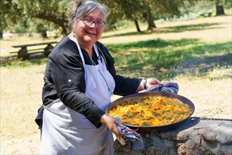 Woman chef with white apron showing her typical Spanish paella cooked on the fire in the