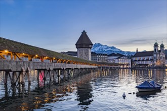 Chapel Bridge at dusk, with view to Pilatus, calm lake with a boat and reflections of the bridge in