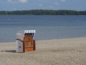 An empty beach chair stands on the sandy beach of a lake under a blue sky with some clouds, lonely