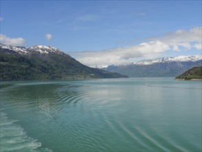 A peaceful lake with wave patterns, surrounded by mountains under a clear sky with some clouds,