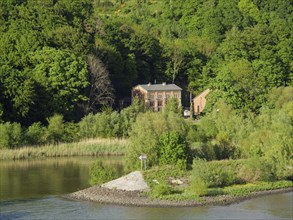 Lonely house surrounded by dense green trees on a riverbank. Surrounded by nature, green bank on a