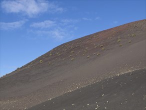 A hill with sparse vegetation under a slightly cloudy sky, barren landscape with roads, craters and