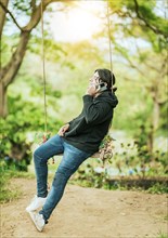 Young man sitting on a swing calling on the phone in a garden. Happy man swinging talking on the