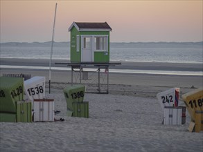 Various colourful beach chairs on a sandy beach with a green beach house in the background at dusk,