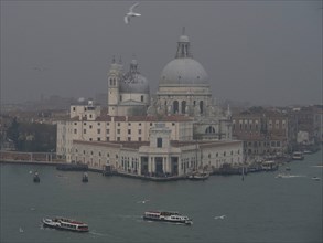 Basilica on the water in Venice, with boats in foggy atmosphere and historic buildings, church