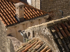 Close-up of rustic rooftops with stone walls and a chimney, highlighting red tiles and textures in