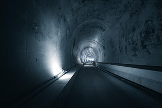 A long tunnel with concrete walls and LED lights on the sides, creating a dark, industrial