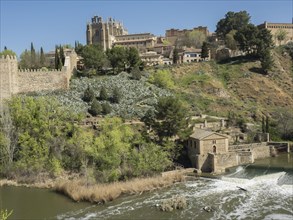 Castle and historical buildings on a hill with river and green vegetation in the foreground on a