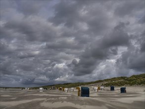Various beach chairs stand in front of a cloudy sky on a deserted beach, colourful beach chairs on