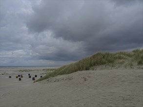 Large dunes and a cloudy sky frame the deserted beach chairs on the beach, colourful beach chairs