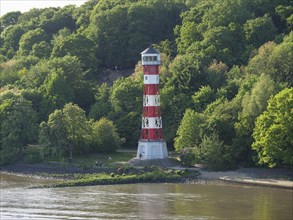 Red and white lighthouse in the middle of a lush, green landscape on the river bank, green bank on
