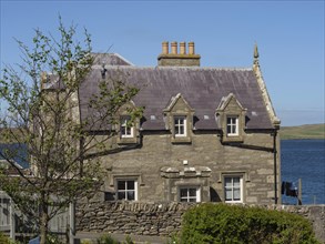 A stone house with fireplaces next to a tree, coastal landscape, blue sky and sea, old stone house