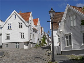 White wooden houses with red tiled roofs along a cobblestone street, street lamp, bright blue sky,