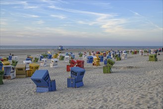 Different coloured beach chairs on a sandy beach at dusk with the sea in the background, many